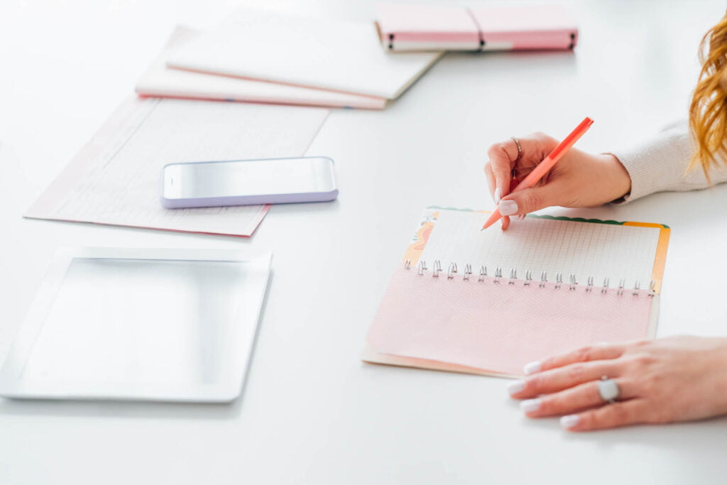 Nainen kirjoittaa muistikirjaan. Tabletti ja älypuhelin.